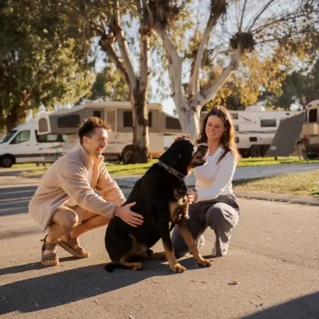 A man and woman patting a large black dog with caravans in the background