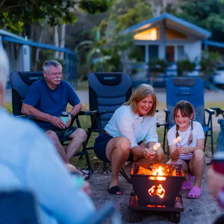 Grandfather, grandmother and granddaughter gathered around a campfire.