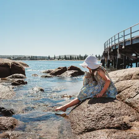 A girl playing in rock pools at Victor Harbor, with a deck in the background.